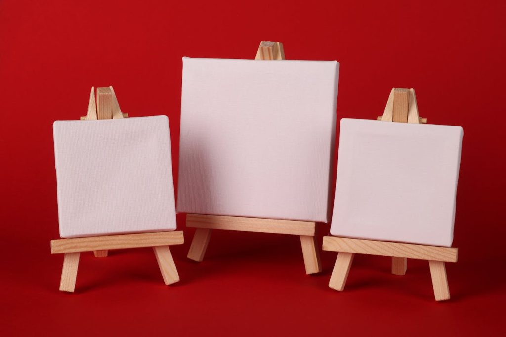 Three small blank art canvases on wooden easels, ready for painting, on a bold red background.