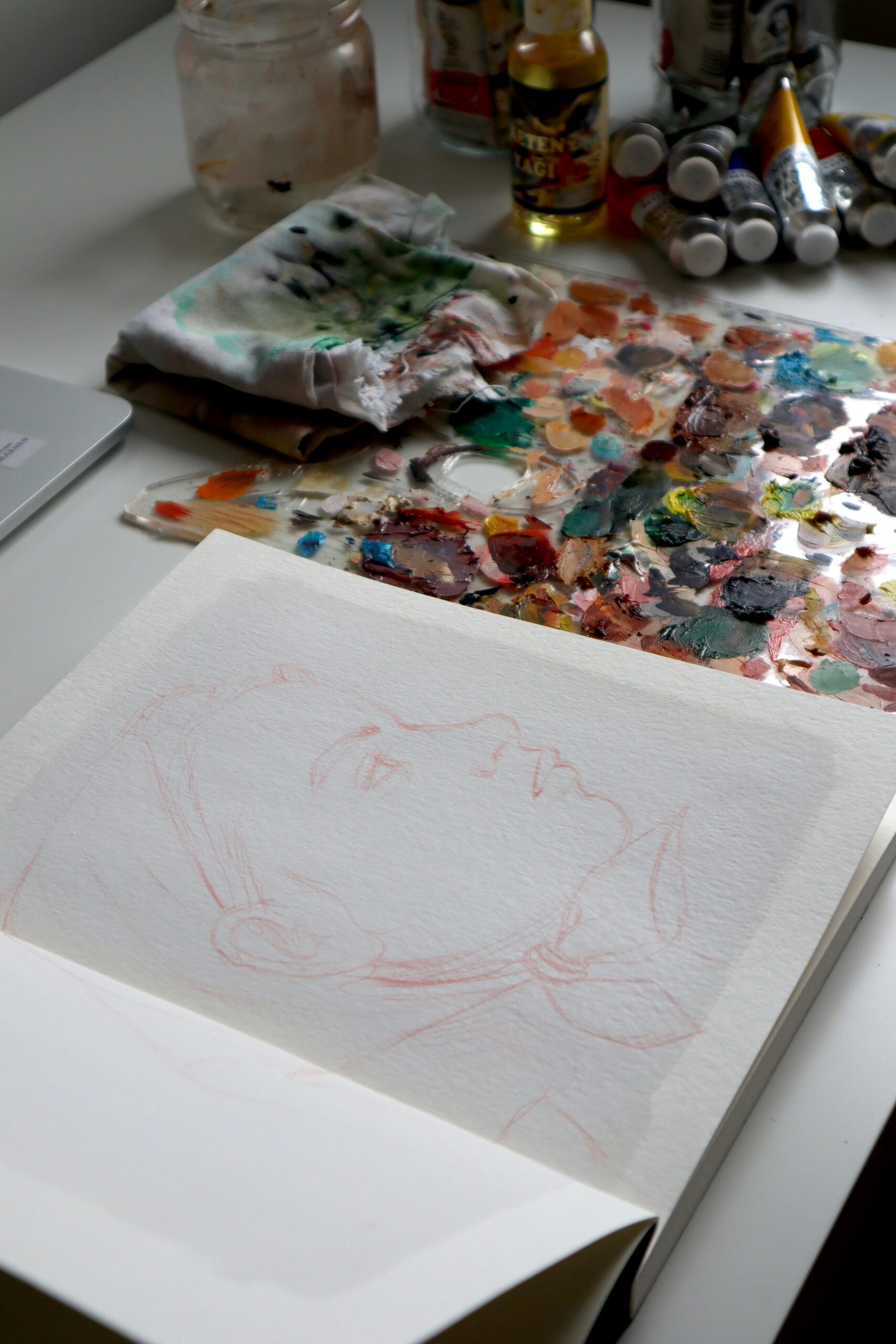 An artistic workspace featuring a sketchpad with a drawing, surrounded by art supplies and colorful paints.